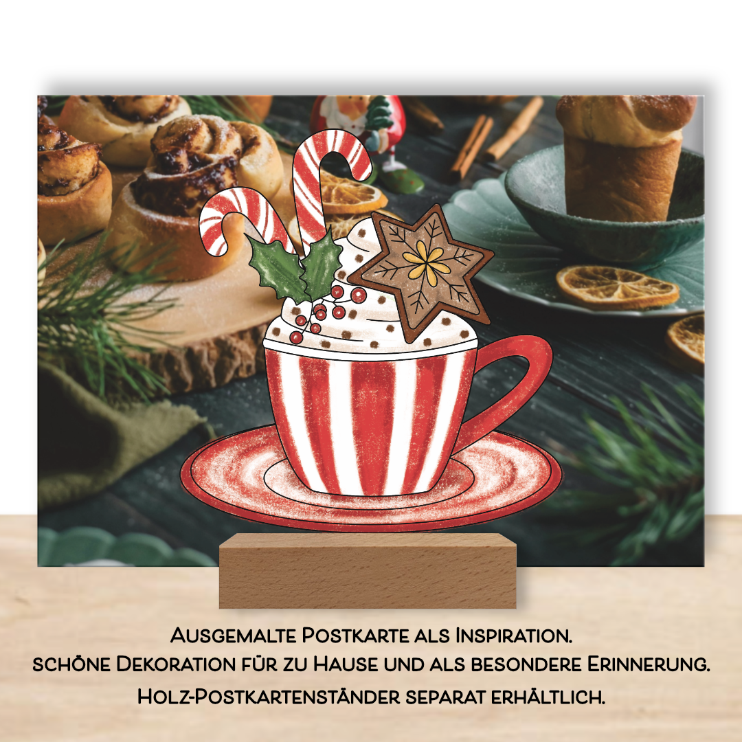 Ausgemalte weihnachtliche Postkarte als Inspiration im Postkartenständer aus dem Postkarten-Set "Glitzerzeit". Das Ausmalbild eine weihnachtliche Tasse ist ausgemalt in rot und weiß und verziert mit einem braunen Lebkuchen, rot weißen Zuckerstangen und einer grünen Mistel.