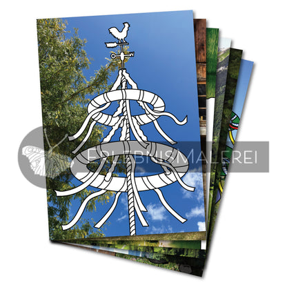Fächerartig aufgefächerte Ausmalkarten aus einem bayerischen Malbuch für Erwachsene und Senioren; im Vordergrund ein stilisierter Maibaum zum Ausmalen vor einem realen Fotohintergrund mit blauem Himmel und grünen Bäumen.