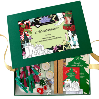 Eine geöffnete dunkelgrüne Geschenkbox mit goldenem Satinband zeigt den ErlebnisMalerei Adventskalender. Auf dem Deckel liegt ein farbenfrohes Etikett mit weihnachtlichen Motiven und dem Hinweis auf „24 kleine Auszeiten zum Innehalten, Ausmalen und Genießen“, als kreative Alternative zum klassischen Malbuch. Im Inneren befinden sich farbige Holzklammern, zwei Teelichter, weihnachtliche Streuteile, ein Holzelement sowie ein kleines Heftchen mit Ausmalüberraschungen. 
