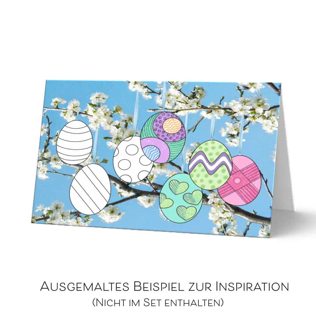 Halb ausgemalte Oster-Grußkarte als Inspirationsbeispiel. Sieben hängende Ostereier auf Fotohintergrund mit  Kirschblütenzweigen vor blauem Himmel. 
Einige noch weiß als Ausmalvorlage zu sehen und andere bereits bunt ausgemalt. Diese Karte dienst als Inspiration und ist nicht im Set enthalten. 