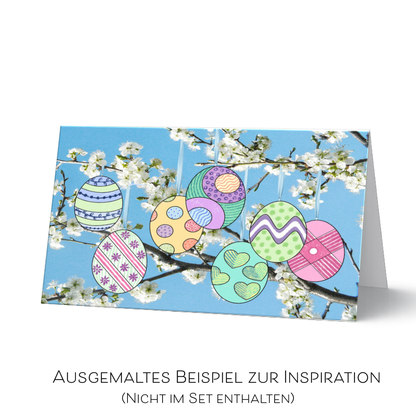 Ostergrußkarte fertig ausgemalt als Inspirationsbeispiel. Sieben bunte Ostereier in verschiedenen Mustern und Farben, hängend an Ästen mit weißen Kirschblüten vor blauem Himmel. 
Die fertig ausgemalte Karte ist nicht im Set enthalten.