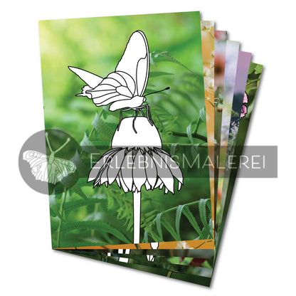Malbuch aus Einzelseiten mit zarten Blütenmotiven – vorne eine Ausmalkarte mit einem Schmetterling auf einer Blume, vor einem lebendigen Fotohintergrund aus frischem Grün; dahinter weitere florale Ausmalmotive aus dem Set Blütenzauber von ErlebnisMalerei.
